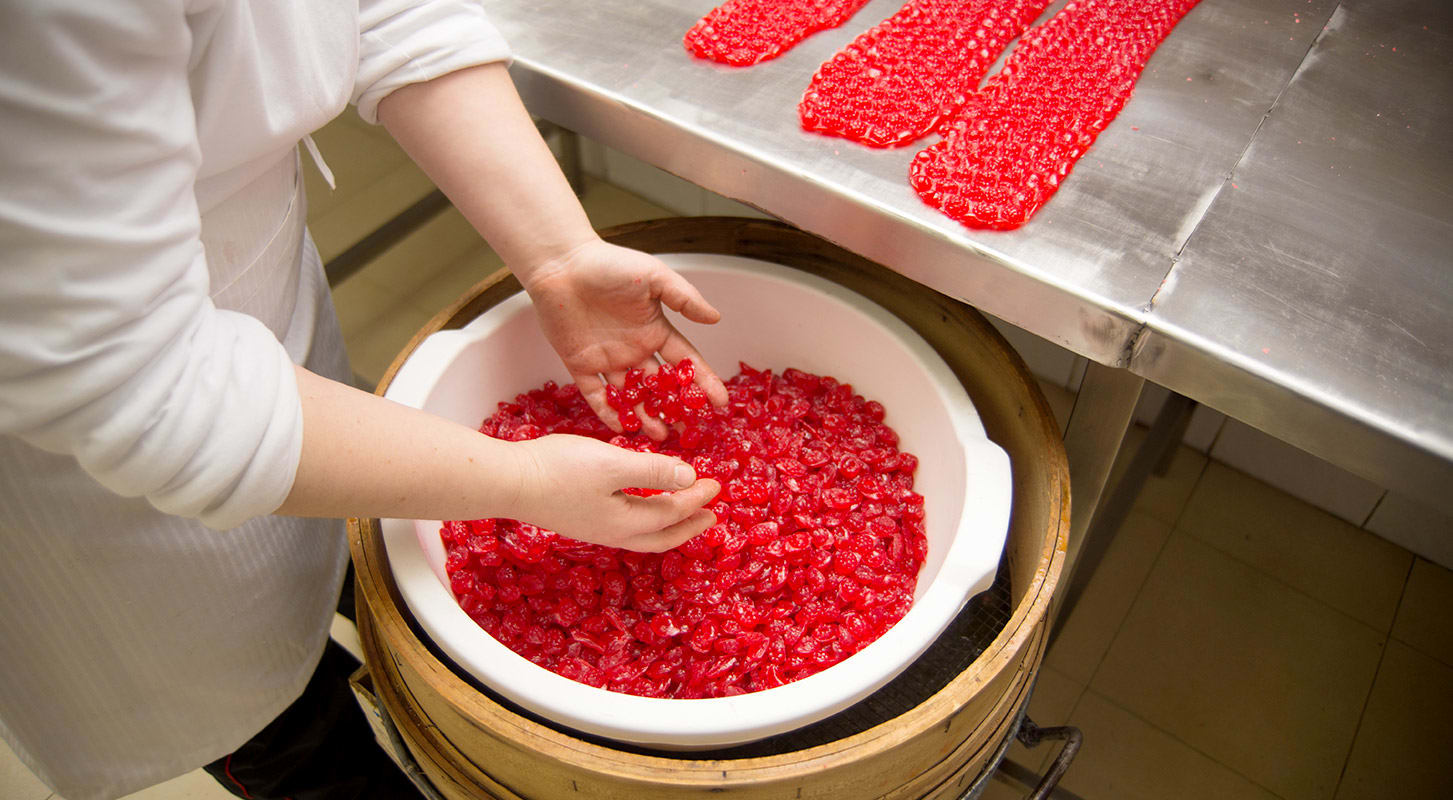A person dressed in a apron prepares vibrant red gummy candies into a large white bowl.